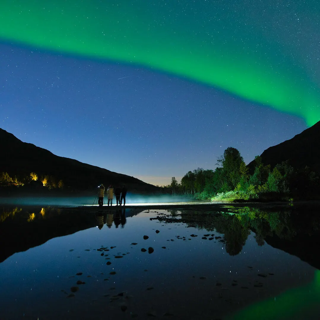 Guests by a lake under the northern lights