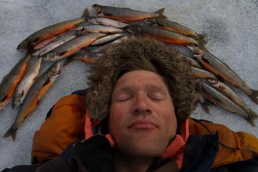 Roy lying in the snow with a row of freshly caught char around his head