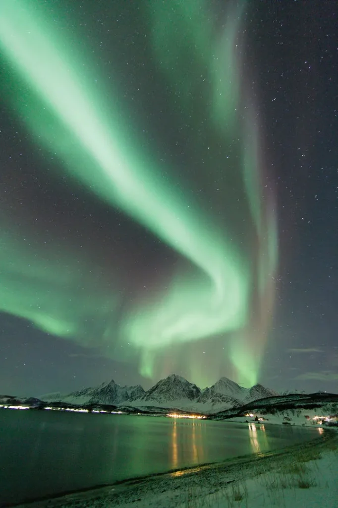 A green aurora curling above a moonlit valley